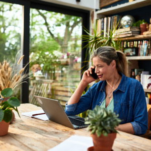 Businesswoman using mobile phone in front of laptop
