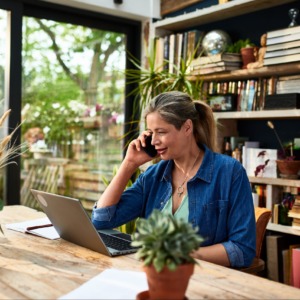 Businesswoman using mobile phone in front of laptop